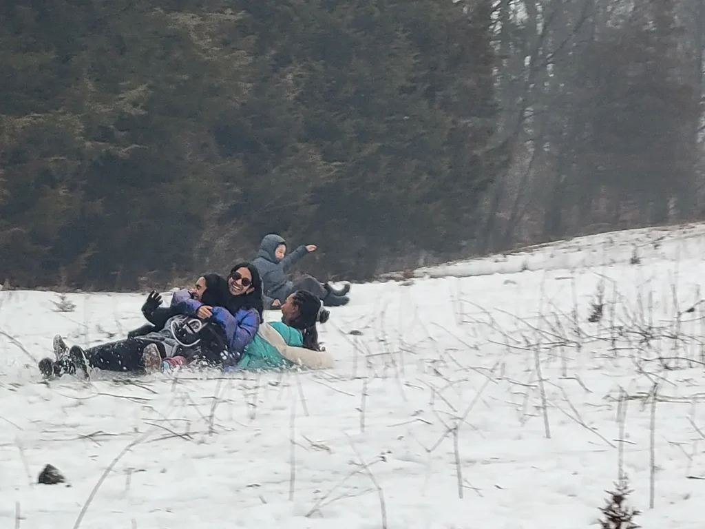 Family sledding down a snowy hillside together, laughing as they slide through winter woods